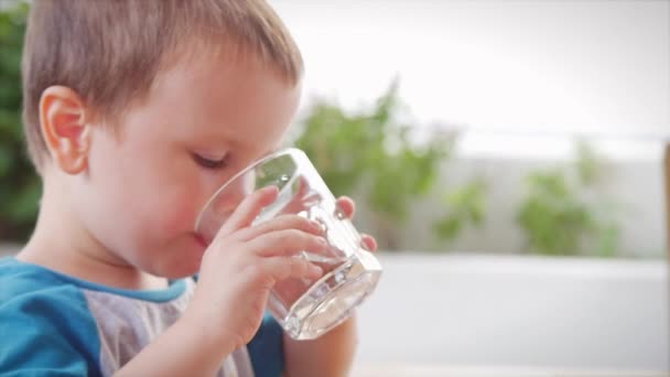 Roztomilý chlapeček pije sklenici vody v kavárně. Zpomal, malý chlapec pije vodu. Detailní záběr. To dítě pije šálek vody..