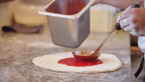 Método de cocción pizza pepperoni, el chef italiano hace pizza italiana real, derrama una salsa roja especial en la masa con un cucharón y lo enrolla en un movimiento circular . — Vídeos de Stock