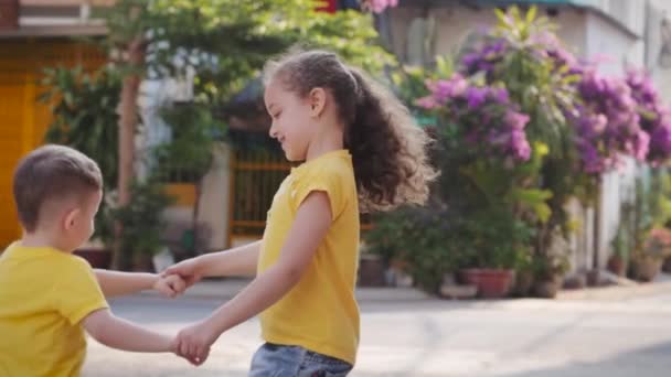 Aktive Mädchen oder Schwester Kindermädchen und niedliche kleine Junge springen tanzen auf der Straße Händchen haltend, glückliche Familie Tochter und Sohn, Kinder genießen Spaß Action-Spiel zusammen. — Stockvideo