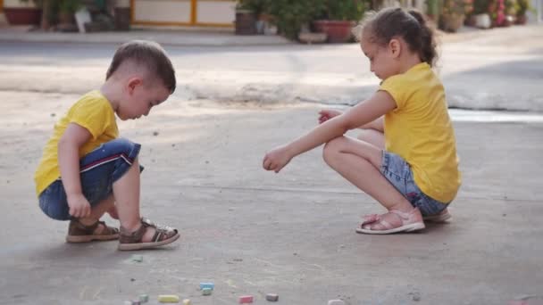 Çocuklar birlikte eğlenceli bir oyun oynamaktan hoşlanırlar. Aktif küçük kız ya da kız kardeş ve dans et. Küçük tatlı çocuk, sokakta pastel boyalarla çizim yapıyor.. — Stok video