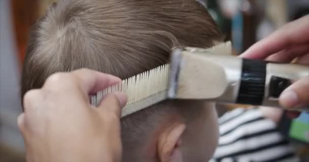 Taglio di capelli per bambini nel salone al momento dell'epidemia di coronavirus. Il bambino si fa tagliare i capelli. Acconciature per bambini. Stylist in una maschera protettiva da covid-19 fa un'acconciatura elegante per un — Video Stock