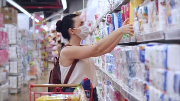 Eine junge Frau mit einer Maske vor einer Coronavirus-Epidemie steht in einem Supermarkt, wo Menschen in Panik All kaufen. Corontin, Isolation von Menschen.