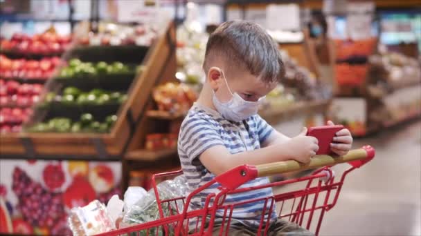 Mutter mit Kindern kauft im Supermarkt ein, das Kind sitzt in einem Einkaufswagen mit Produkten und guckt Cartoons auf dem Smartphone.