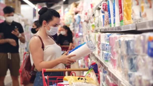 Junge Frau in Maske von einer Coronavirus-Epidemie kauft im Supermarkt ein, wählt Toilettenpapier, Menschen in Panik vor der globalen Epidemie kaufen alles auf.