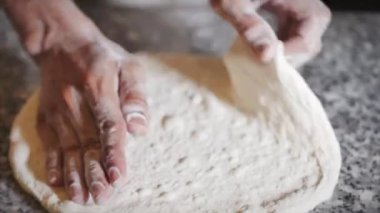 İtalyan aşçı pizza hazırlıyor, hamuru un kaplı bir yüzeyde yapıyor ve elleriyle yoğuruyor.