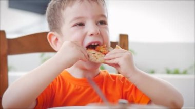 Çocuk kafesinde otururken İtalyan pizzası yiyen tatlı, sağlıklı bir anaokulu çocuğu. Mutlu çocuk hevesle bir restoranda İtalyan pizzası yiyor ve ondan hoşlanıyor. Çocukluk, sağlık konsepti.