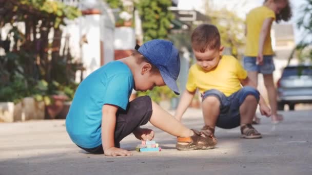 Zabawne małe dzieci lubią grać w zabawną grę razem, co rysunki z kolorowych kredek, przedszkolaków z pięknym uśmiechem, aktywnych małych dzieci uruchomić rysunek z kredek na asfalcie na ulicy. — Wideo stockowe