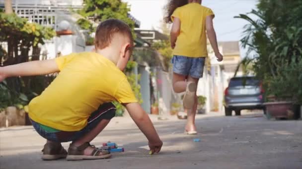 Zabawne małe dzieci lubią grać w zabawną grę razem, co rysunki z kolorowych kredek, przedszkolaków z pięknym uśmiechem, aktywnych małych dzieci uruchomić rysunek z kredek na asfalcie na ulicy. — Wideo stockowe