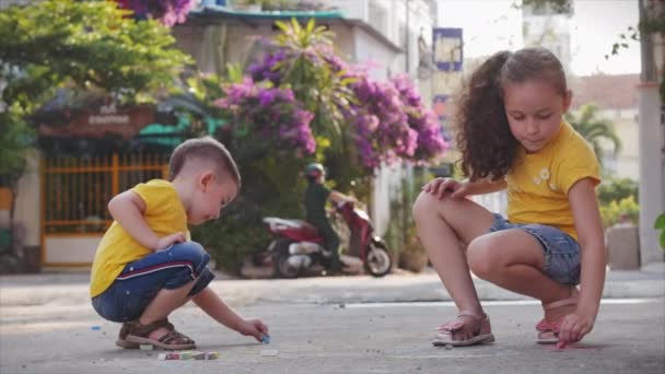 Grappige kleine kinderen spelen graag samen een leuk spelletje, maken tekeningen met gekleurde krijtjes, kleuters met een mooie glimlach, actieve kleine kinderen lopen op straat met krijtjes op asfalt te tekenen. — Stockvideo