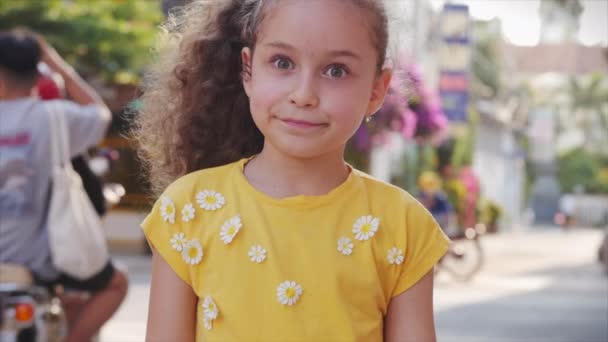 Vicces kislány mosolyog, nézi a kamerát az utcán, egy aranyos gyerek játszik az utcán, rajzokat készít színes krétákkal az öröm, egy óvodás egy gyönyörű mosollyal.