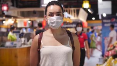 Coronavirüs salgınından maske takmış genç bir kadın marketin market bölümünde duruyor. İnsanlar panik içinde yiyecek alıyor..