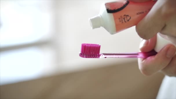 Выстрел женских рук, сжимающих цветную зубную пасту на розовую зубную щетку. Гигиена полости рта в современной ванной комнате. Крупный план . — стоковое видео