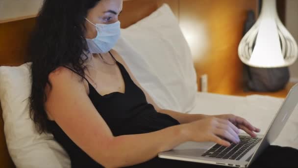 Freelancer vrouw in een masker van een coronavirus epidemie werk is verantwoordelijk voor belangrijke taak op freelance e-mail thuis typen op laptop, geobsedeerd werk-gericht meisje met behulp van computer voor online werk. — Stockvideo