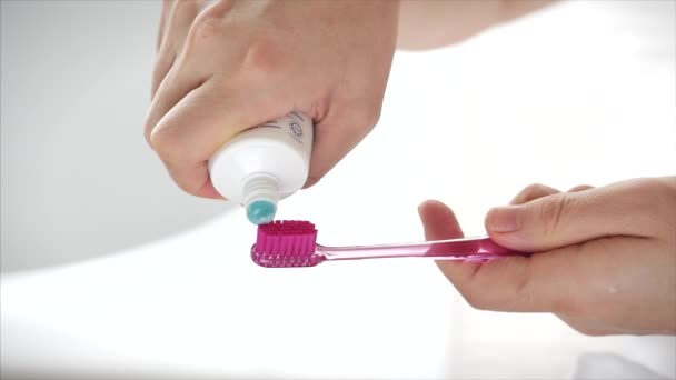 Un colpo di mani femminili che strizzano dentifricio colorato su uno spazzolino rosa. Igiene orale in un bagno moderno. Primo piano . — Video Stock