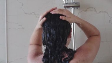 Güzel genç bir kadın sıcak bir duş deresinin altında durarak saçındaki şampuanı temizler. Saç ve vücut temizliği kavramı, hijyen..