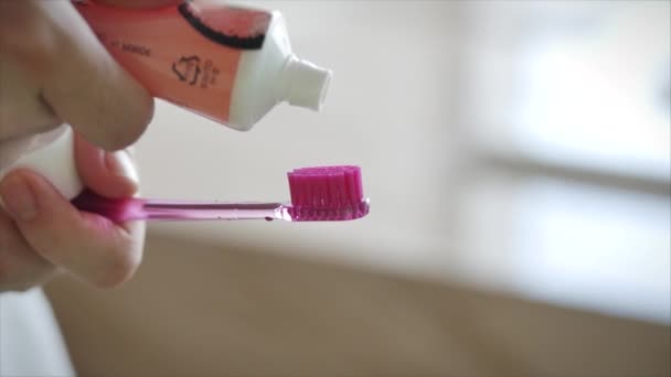 Tiro de manos femeninas apretando pasta de dientes de color sobre un cepillo de dientes rosa. Higiene bucal en un baño moderno. Primer plano . — Vídeo de stock