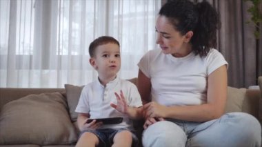 Sevimli bir aile, mutlu bir anne ve tatlı bir çocuk. Tablet bir cep telefonunun ekranına bakarlar. Çocuklu bir anne, evde kanepede oturur, akıllı telefon kahkahalarıyla oynar..