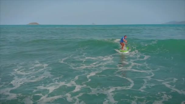 Surfista voa na crista de uma onda, um surfista controla o remo, de pé em uma prancha de surf. Surfista está esperando por sua onda. — Vídeo de Stock