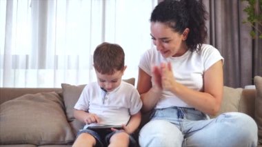 Sevimli bir aile, mutlu bir anne ve tatlı bir çocuk. Tablet bir cep telefonunun ekranına bakarlar. Çocuklu bir anne, evde kanepede oturur, akıllı telefon kahkahalarıyla oynar..