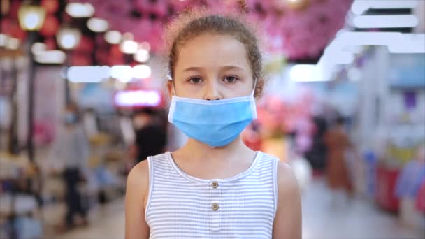 コロナウイルスやウイルスの流行からかわいい女の子は、パニックになって買い物をしているウイルスの仮面の人々の中にカメラを見ています。コロンチン人の隔離. — ストック動画