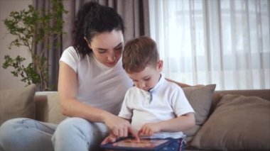 Sevimli bir aile, mutlu bir anne ve tatlı bir çocuk. Tablet bir cep telefonunun ekranına bakarlar. Çocuklu bir anne, evde kanepede oturur, akıllı telefon kahkahalarıyla oynar..