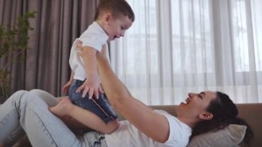 Mutlu sağlıklı bir aile, genç bir anne, küçük tatlı bir çocuğu kaldırıyor. Evdeki kanepede uçuyor. Komik çocuk, annesinin antrenmanında..