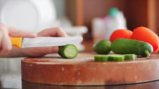 Filha ajuda a mãe a cozinhar na cozinha, as mãos de uma menina de 6-7 anos de idade faz uma faca cortando tomates e pepinos para salada. Close-up na cozinha crianças mãos cortadas em vegetais frescos em — Vídeo de Stock