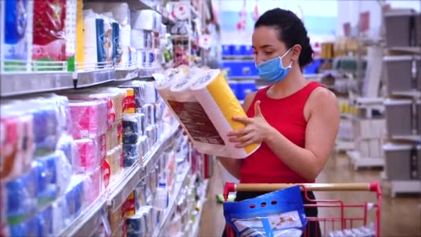 Egy fiatal nő egy koronavírus járvány álarcában vásárol egy szupermarketben, vécépapírt választ, az emberek pánikba esnek a világjárványtól, és mindent felvásárolnak..