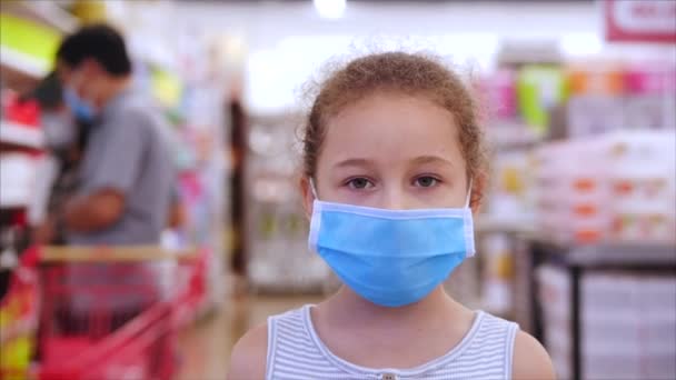 Милая маленькая девочка от эпидемии коронавирусов или вирусов смотрит в камеру среди людей в масках от вируса, которые делают покупки в панике. Коронтин, изоляция людей. Эпидемический Ковид-19 — стоковое видео