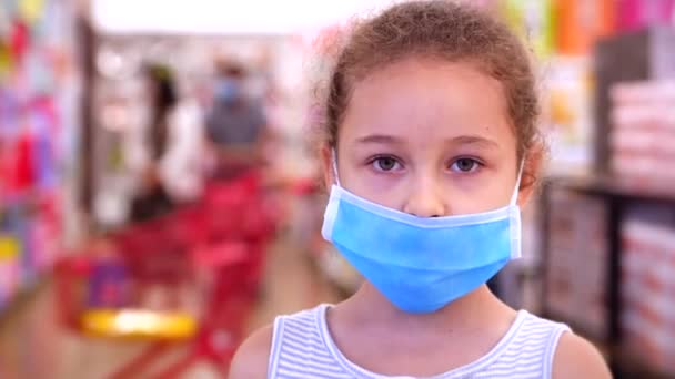 Linda niña de una epidemia de coronavirus o virus mira a la cámara en medio de personas enmascaradas del virus que están de compras en un pánico. Corontin, aislamiento de la gente. Covid-19 epidémico — Vídeo de stock