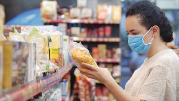 Eine junge Frau mit einer Maske vor einer Coronavirus-Epidemie steht in der Lebensmittelabteilung eines Supermarktes. Sie kauft schnell Lebensmittel ein, wo die Menschen in Panik Lebensmittel kaufen.