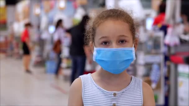 Klein meisje kind in een masker van virussen van de epidemie van het coronavirus of virussen kijkt naar de camera bij mensen met maskers, die rijden de kassa vol met voedsel karren. Corontin, isolatie — Stockvideo