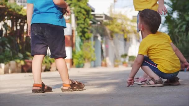 Funny little children, preschoolers play, make drawings with colored pencils together, draw with colored pencils crayons on the asphalt on the street. — Stock Video