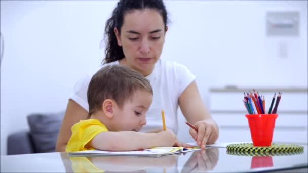 Mãe feliz aprendendo bebê bonito menino jogando jogos de tabuleiro em casa, mãe ajuda bebê filho aprender a desenhar com lápis juntos desfrutar do processo criativo. Covid-19, proteção do vírus, pandemia em palavra — Vídeo de Stock