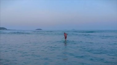 Sörfçü dalgasının sörf yapmasını bekliyor sörfçü sörf tahtasında dururken küreği kontrol ediyor. Sörfçü dalgasını bekliyor..