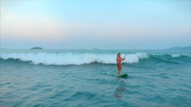 A szörfös egy hullám tetején repül, egy szörfös irányítja az evezőt, egy szörfdeszkán állva. A szörfös várja a hullámát.. — Stock videók