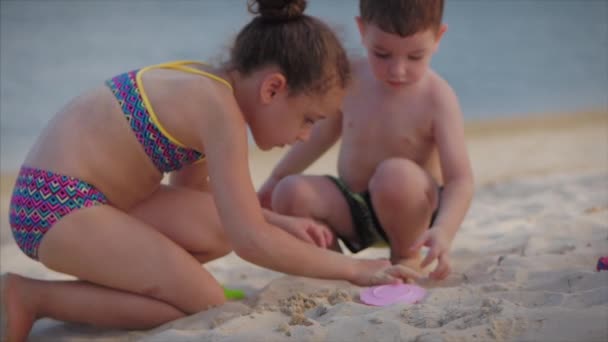 Des enfants drôles, heureux et insouciants jouant au bord de la mer avec du sable. Enfants jouant, frère et sœur jouant au bord de la mer. Bonne enfance . — Video