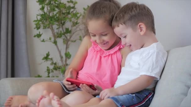 Crianças felizes brincando em casa relaxante usar um smartphone abraçando sentar-se no sofá filha e filho, olhar para a tela de um telefone celular, assistir desenhos animados. — Vídeo de Stock