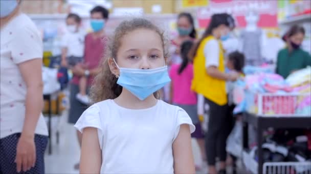 Милая маленькая девочка от эпидемии коронавирусов или вирусов смотрит в камеру среди людей в масках от вируса, которые делают покупки в панике. Коронтин, изоляция людей. — стоковое видео