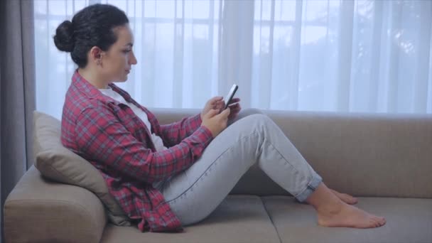 Junge ernsthafte Freiberuflerin, die an einem Laptop arbeitet, zu Hause auf einem Sofa sitzend, Geschäftsfrau, die auf einem Laptop tippt, fokussiertes Mädchen, das einen Computer benutzt, um zu Hause Online-Arbeit zu studieren. Arbeitskonzept für Hausangestellte — Stockvideo