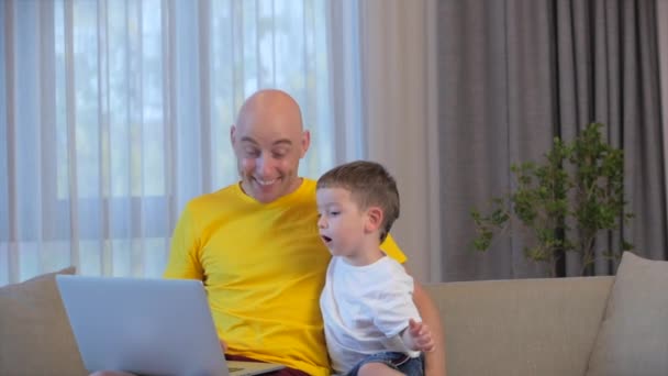 Man frilansare arbetar på en bärbar dator sitter på en soffa hemma, affärsman skriva på en bärbar dator, med hjälp av en dator för att studera online-arbete hemma, hans son närmar sig honom och kramar sin far trött på arbete. — Stockvideo