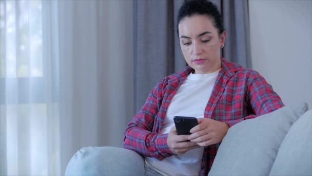 Jonge serieuze vrouw werken freelancer typen op de telefoon zitten op de bank thuis, zakenvrouw zit thuis types op smartphone controles mail naar online werk te studeren thuis. — Stockvideo