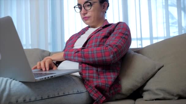 自宅のソファに座ってノートパソコンで働く若い深刻な女性のフリーランス、ノートパソコンを入力する実業家の女性、自宅でオンライン作業を勉強するためにコンピュータを使用して焦点を当てた女の子。家事事務員の仕事のコンセプト — ストック動画