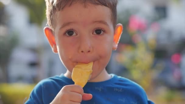 Маленький голодный мальчик ест мороженое, глядя в камеру на фоне природы красивых гор и синего моря. Детское личико смазано мороженым . — стоковое видео
