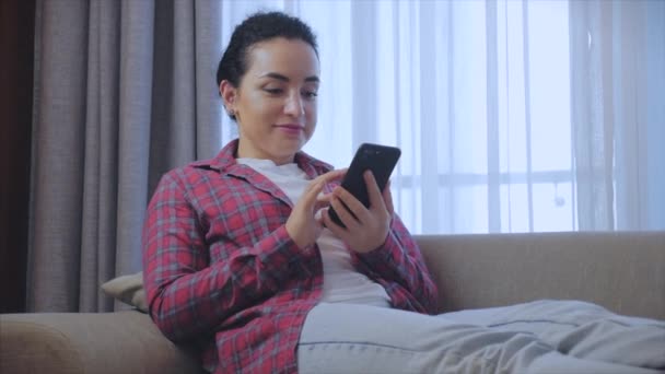 Joven mujer seria freelancer trabajando en una computadora portátil sentada en un sofá en casa, mujer de negocios escribiendo en una computadora portátil, chica enfocada usando una computadora para estudiar trabajo en línea en casa. Concepto de trabajo del empleado doméstico — Vídeos de Stock