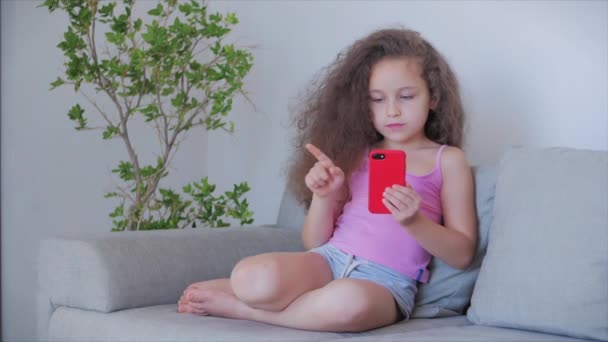 Zvědavý roztomilý chlapec předškolní dítě pomocí digitálního tabletu technologie zařízení vypadá telefon.Hraje v telefonu sedí na pohovce sám.. — Stock video