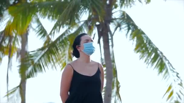 Portret van jonge vrouw in een masker van een coronavirus epidemie draagt beschermende vraag in de straat.Vrouw staat zwarte jurk weg te kijken.Concept gezondheid en veiligheid leven, Covid-19, pandemie in woord. — Stockvideo