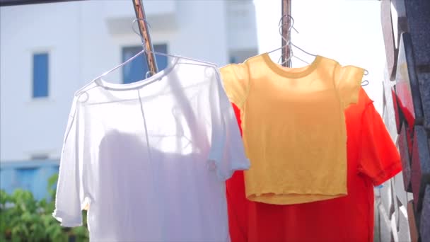 Після прання білизна і одяг сушать після прання на лінії одягу, футболки, рожевий одяг, жовті, яскраві кольори сушать на контурі одягу на відкритому повітрі в сонячну погоду . — стокове відео