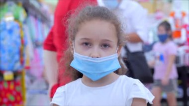 Koronavirüs ya da virüs salgınından maskeli bir çocuk panikle alışveriş yapan maskeli insanların arasında kameraya bakar..