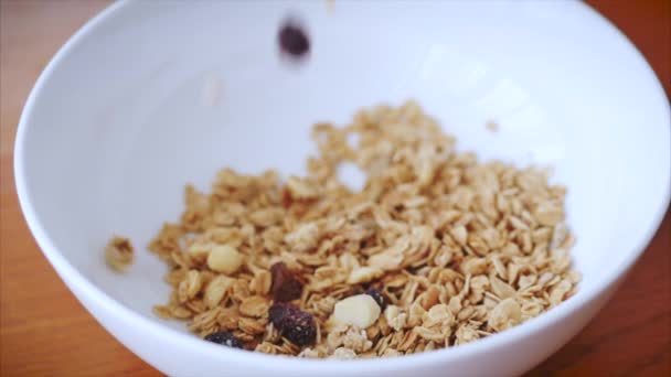 Kahvaltılık tabağa düşen gevrek gevrekleri yavaş çekimde. Kahvaltı konsepti, sağlıklı bir diyet, kaju fıstıklı granola ve ahududu dilimleri ve kuru üzüm.. — Stok video